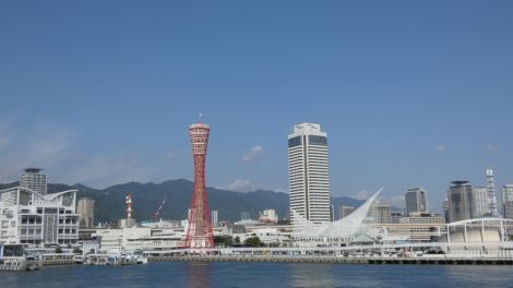 Zdjęcie nr 3 (13)
                                	                             Zdjęcie Tomasza Jakutowicza z pobytu w Japonii. Zdjęcie przedstawia wybrzeże, wysokie budynki, czerwona wieża, w tle niebieskie niebo i góry.
                            