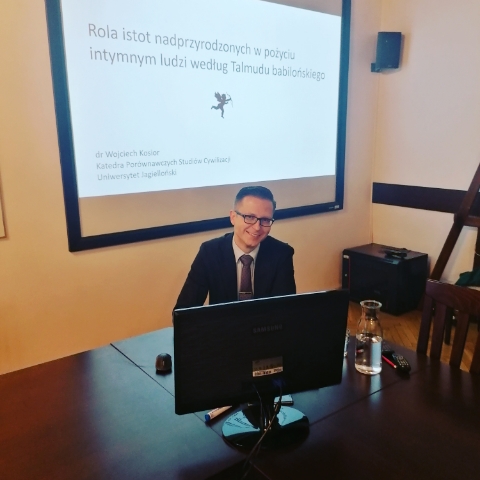 Zdjęcie przedstawia doktora Wojciecha Kosiora w trakcie wykładu. W tle slajd z prezentacji z tytułem wystąpienia i afiliacją.